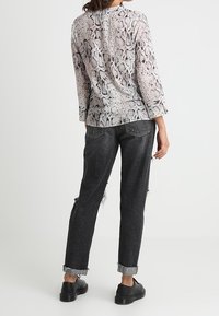 Haut à manches longues avec imprimé serpent en gris et beige, assorti à un jean noir déchiré et des chaussures à plateforme noires. Détails incluant des poignets retroussés.