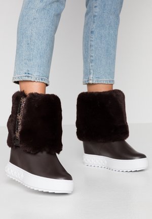 Jambes en jean bleu clair portant des bottines marron foncé avec des semelles blanches épaisses et des cols en fausse fourrure pliés.