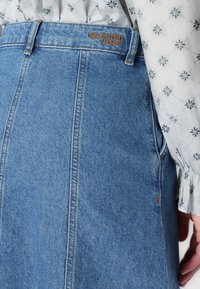 Denim krilo v svetlo modri barvi z visokim pasom, vidnimi šivi in oznako blagovne znamke "SELECTED FEMME" blizu vrha. Vsebuje stranko.