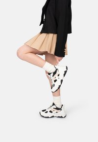 Schwarze und beigefarbene Sneaker aus Mesh und strukturiertem Stoff mit einer klobigen Sohle, weißen Schnürsenkeln und einem schwarzen Akzentmuster.