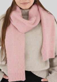 Écharpe tricotée rose clair avec des extrémités côtelées, en matériau doux, drapée autour d'un cou, associée à un pull beige.