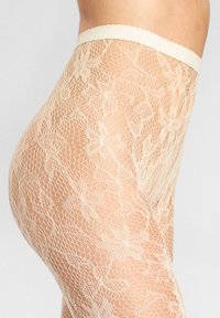 Nude koronkowe rajstopy z kwiatowym wzorem, z falbaniastym pasem i przezroczystym, teksturowanym materiałem, dające delikatny wygląd.