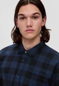 Langsleeve overhemd met knopen in donkerblauw en zwart geruit patroon, voorzien van een borstzak en een klassieke kraag. Zachte stoftekstuur.