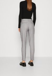 Kostkované kalhoty v šedé a bílé barvě, s úzkým střihem a zadními kapsami, doplněné černými botami. Hladká tkanina s upraveným vzhledem.