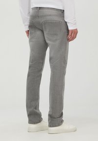 Jeans in denim grigio con un fit dritto, caratterizzati da due tasche posteriori e un design pulito e minimalista. Indossati con scarpe da ginnastica bianche.