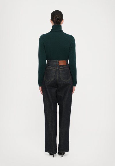 Groene coltrui gecombineerd met donkergekleurde spijkerbroek met hoge taille, voorzien van een tan leren pat op de achterkant en een losse pasvorm.