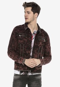 Rote, ausgefranste Jeansjacke mit silbernen Nägeln an den Schultern und Taschen, zwei mit Reißverschluss versehenen Brusttaschen und einer verkürzten Passform.