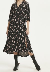 Svart omslagsklänning med paisleymönster i rosa och vitt, trekvartslång ärm, sidoklyvning och detalj med spänne i midjan.