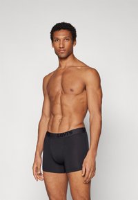 Fekete pamut boxer alsónadrág fekete Levi's logós derékkal, testhez simuló kialakítással és sima textúrával. Nincsenek látható minták vagy díszítések.