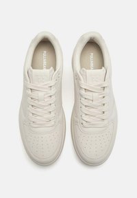 Pantofi sport albi cu glezna joasă, design perforat, piele texturată, șireturi plate și logo în relief pe limbă. Aspect moale, minimalist.