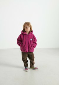 Lyserød fleece zip-up hættejakke med hætte og forlommer, parret med brune kordfløjl bukser og multicolor ternede sneakers.