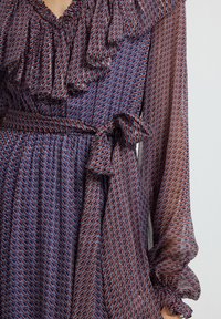 Rimpeljurk in donkerblauw met rode en witte geometrische patronen. Voorzien van lange mouwen en een strikceintuur voor een getailleerde uitstraling.