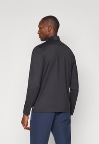 Schwarzes Langarm-Polohemd mit Stehkragen, glatter Textur und einem dezenten Logo-Detail, kombiniert mit marineblauen Hosen.