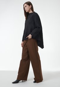 Top negro texturizado con un cuello alto, combinado con pantalones marrones holgados y zapatos de tacón alto negros, resaltando una silueta moderna.