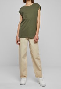 Olivově zelené tričko s krátkým rukávem z bavlny s ohrnutými manžetami, doplněné o světlé béžové kalhoty s širokými nohavicemi a bílé tenisky. Jednoduchý design, jemná textura.