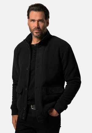 Chaqueta de forro polar negra con cuello con cremallera, botones en el frente y dos bolsillos. Textura suave, diseño informal y ajuste entallado.