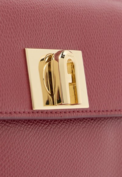 Крупен план на златист катарама Furla върху текстурирана розово-розова кожена чанта.
