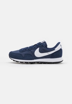 Chaussure de running Nike bleu marine et blanche avec des détails en suède et en tissu, logo swoosh blanc et semelle en caoutchouc noire, vue de côté.