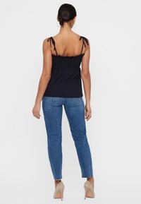 Marineblaue ärmellose Bluse mit verstellbaren gebundenen Trägern und strukturierter Brust, kombiniert mit hellblauen, figurbetonten Jeans und nudefarbenen High Heels.