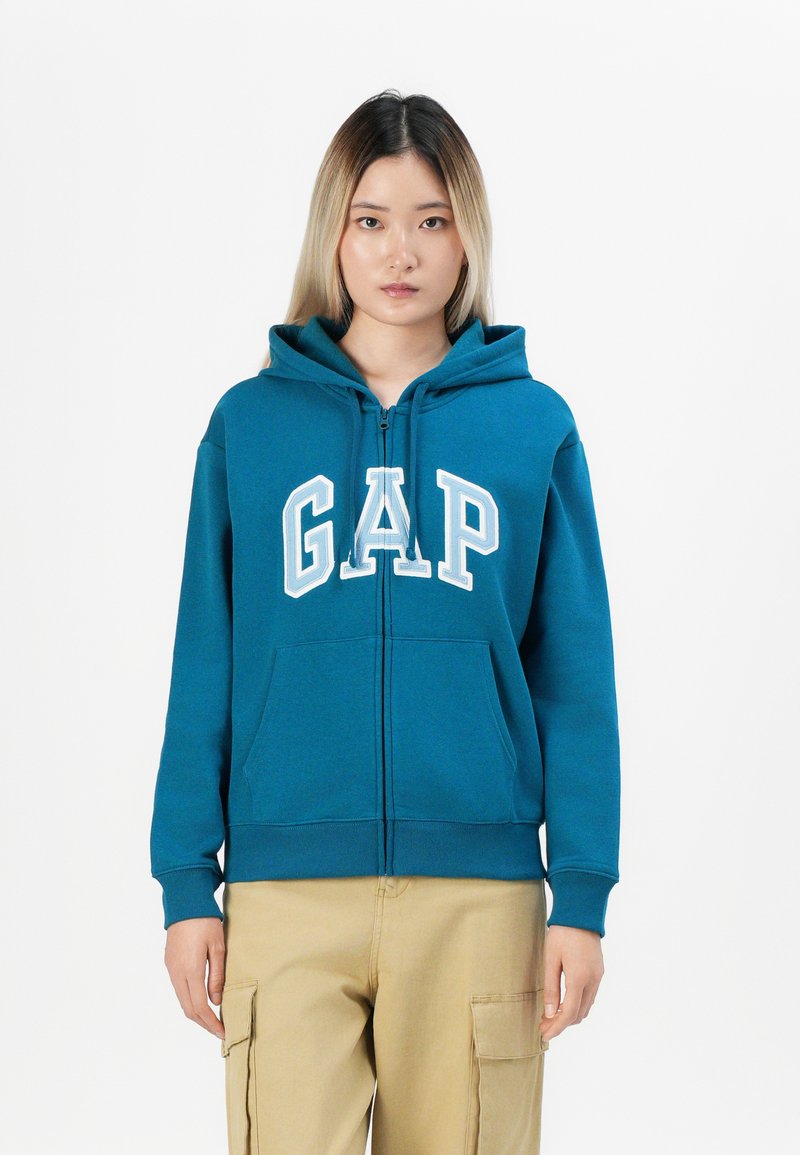 Teal zip-up hoodie with front pockets and white "GAP" lettering. Features a drawstring hood and ribbed cuffs at sleeves and hem.