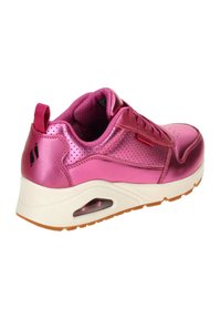 Zapatilla sintética rosa con parte superior brillante, acentos perforados, cuello acolchado y media suela blanca con un cojín de aire visible. Suela de goma marrón.