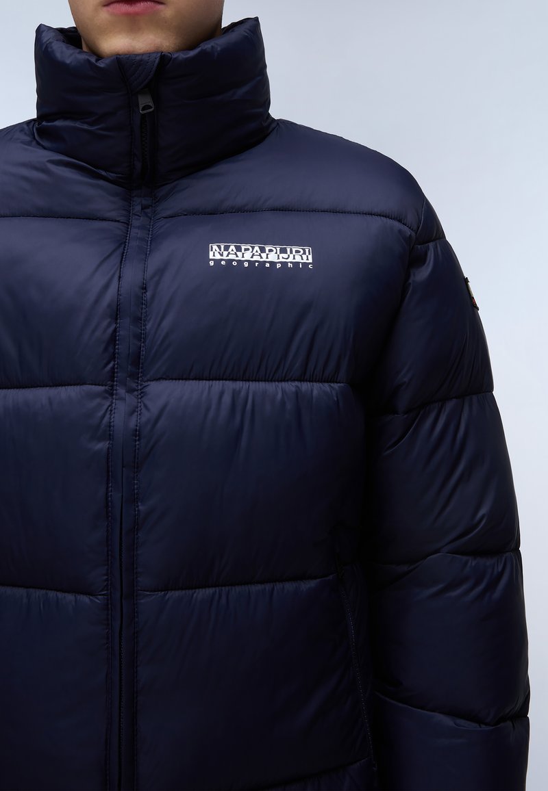 Granatowa kurtka puchowa z wysokim kołnierzem, z przeszyciami, zamkiem błyskawicznym z przodu i białym logo w lewym górnym rogu. Materiał teksturowany i wyściełany.