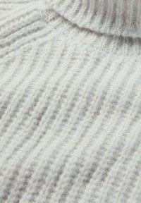Nahaufnahme von einem weichen, weißen gerippten Strickstoff mit einem gefalteten Kragen, der seine flauschige Textur und das gemütliche Material zeigt.