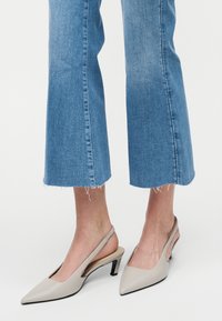 Πόδια με κοντά μπλε τζιν και μπεζ ψηλοτάκουνα slingback με μυτερή μύτη και λεπτά μαύρα μεσαίου ύψους τακούνια σε λευκό φόντο.