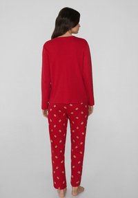 Top rojo de manga larga combinado con pantalones rojos con estampados florales. La tela parece suave, con un ajuste relajado. Sin herrajes ni adornos visibles.