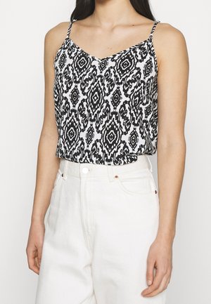 Camicetta a righe in bianco e nero con spalline sottili, design a scollatura a V, tessuto leggero, indossata con pantaloni bianchi a vita alta.
