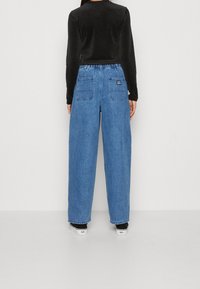 Blå denimbyxor med vida ben och hög midja, med två bakfickor och en svart etikett. Stylad med en svart långärmad skjorta.