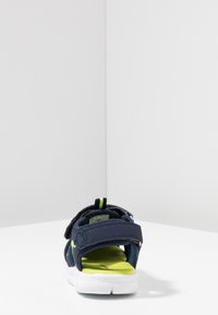 Navy blue sandal with adjustable Velcro straps, green accents, and a cushioned yellow insole. Lightweight rubber sole for comfort.
