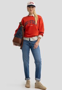 Punane dressipluus, millel on "BIG STAR JEANS" trükk, teksapüksid, beežid tossud ja beebikapuuts, millel on tumesinine serv. Pruun ja tumesinine õlalöö. 