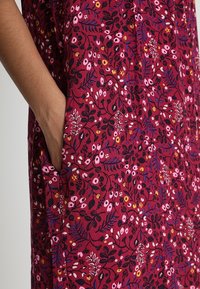 Rød blomsterkjole med et levende mønster i pink, gul og sort. Inkluderer sidelommer og et blødt, tekstureret stof.