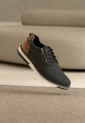 Scarpe da uomo in materiale sintetico blu navy con dettagli in pelle marrone, dotate di cerniera laterale, suola bianca e superficie superiore texturizzata.