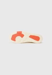 Shoe outsole featuring a textured light cream base with an orange accent and patterned grip design for enhanced traction.