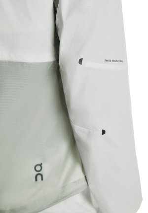 Veste gris clair avec un panneau en mesh, inscription « Swiss Engineering » et accents noirs. Le matériau semble léger et lisse.