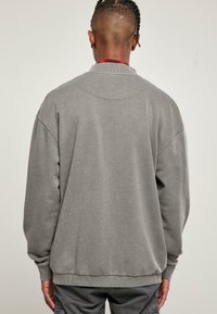 Grå sweatshirt med rundad krage, sänkta axlar och ribbade muddar. Slät yta med lös passform. Inga synliga logotyper eller mönster.