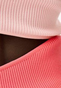 Rosa och korallfärgad ribbad tyglayer, med texturerade mönster och mjukt, stretchigt material, mot en mörk bakgrund.