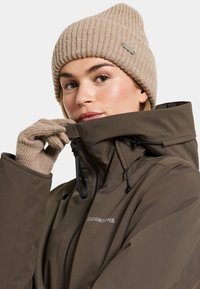 Brown waterproof jacket with high collar, paired with a beige ribbed beanie and matching gloves, featuring a zip closure and adjustable cord.