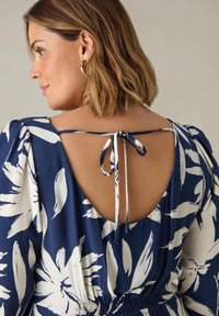 Modrá květinová šaty s otevřeným zadním dílem na zavazování, puffovými rukávy a nařaseným pasem. Vyrobeno z lehké tkaniny s hladkou texturou.