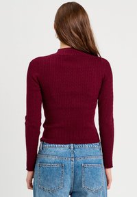 Bordeaux ribbet striktrøje med lange ærmer, høj hals og struktureret mønster, båret med lyseblå højtaljede jeans.