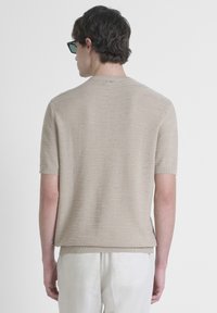 Suéter de punto beige de manga corta con patrón texturizado, escote redondo y dobladillo acanalado. Combinado con pantalones de color claro.