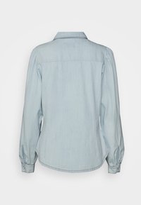 Světle modrá košile s dlouhými rukávy vyrobená z denimu. Má špičatý límec, knoflíkové manžety a zakřivený lem s detailem zadního štítku.