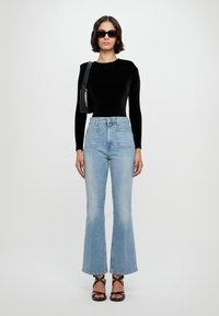 Body de manga larga negro, jeans acampanados azul claro, sandalias negras con tiras. Los accesorios incluyen un pequeño bolso negro de hombro y gafas de sol.