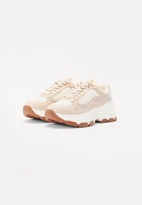 Beige Sneaker mit Mesh- und Lederdetails, ausgestattet mit einer klobigen weißen Sohle mit braunen Akzenten und einem abgerundeten Schuhdesign.