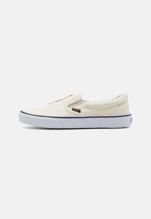 Kremowy sneaker typu slip-on z białą podeszwą, czarnym paskiem i małą czarną metką z napisem "POLO" po boku.