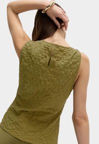 Olivegrön ärmlös topp i texturerat tyg, med nyckelhål bak och en avslappnad passform. Slät finish vid kanterna.