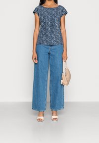 Top a righe navy con maniche corte, abbinato a jeans a gamba larga blu. Una borsa di colore beige chiaro e tacchi aperti completano il look.