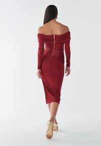 Červené midi šaty bez ramienok vyrobené z jemného materiálu, s naťahovaním a zadným zipsom. Skombinované s zlatými sandálmi na pásiky.